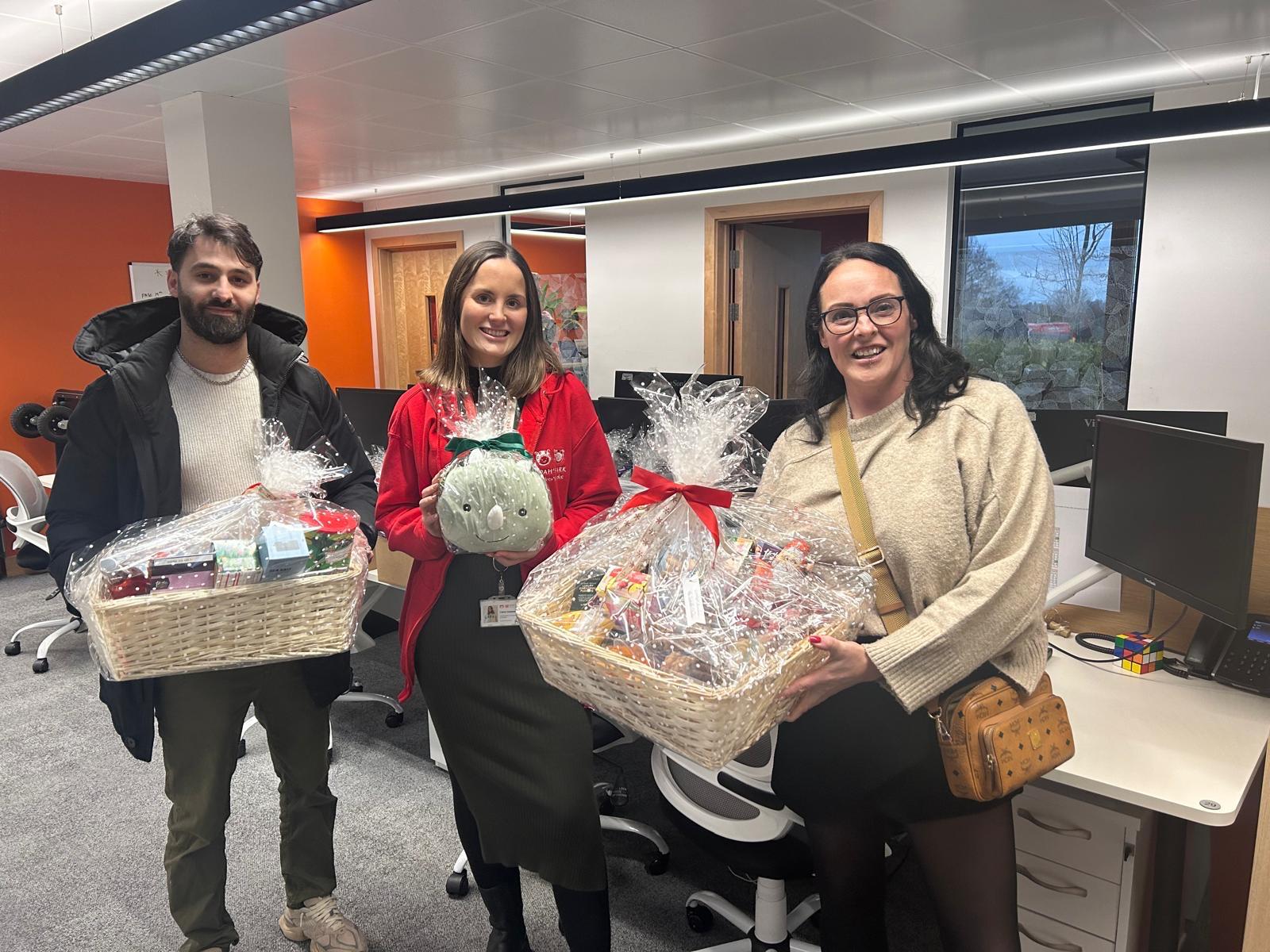 Construction Collective team and Noah's Ark Children's Hospice representatives exchanging wrapped Easter gift baskets and hampers in the Barnet office
