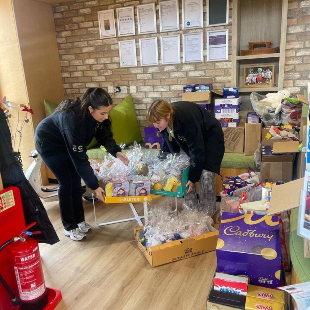 Two Construction Collective team members arranging wrapped Easter gift baskets at Noah's Ark hospice