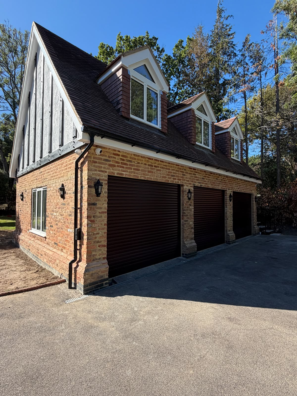 Daytime corner view of the completed Totteridge garage conversion with brickwork, three garage doors and dormer windows